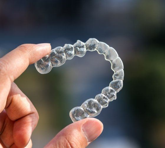Person holding an Invisalign clear aligner in their hand