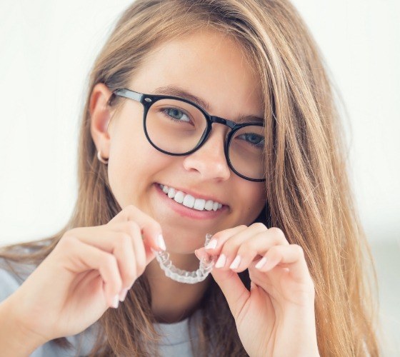 Smiling young woman holding an Invisalign Teen clear aligner