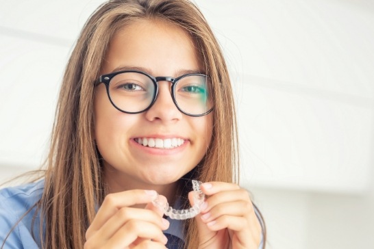Smiling teenage girl holding an Invisalign clear aligner